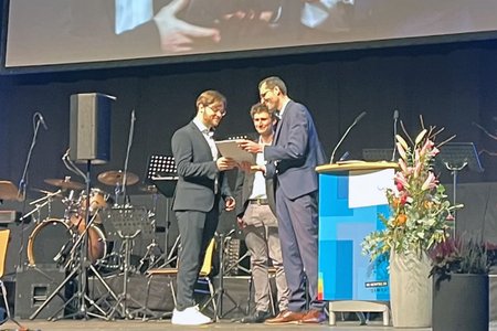 Auf der Bühne der BigBox erhält ein Absolvent den Preis der schwäbischen Wirtschaft; im Hintergrund ein weiterer Preisträger.