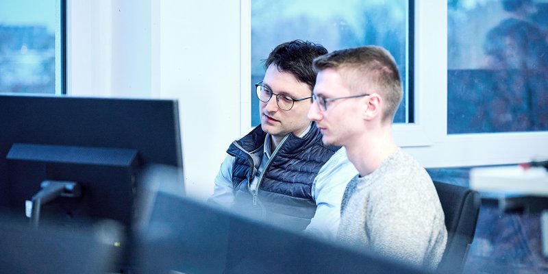 Zwei Männer arbeiten konzentriert an einem PC in einem modernen Büro der Hochschule Kempten