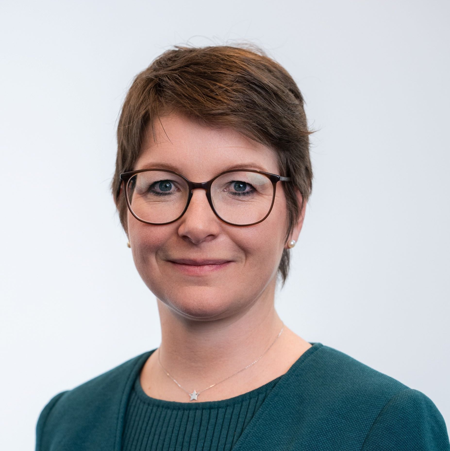 Portrait einer Frau mit kurzen braunen Haaren und Brille im Blazer