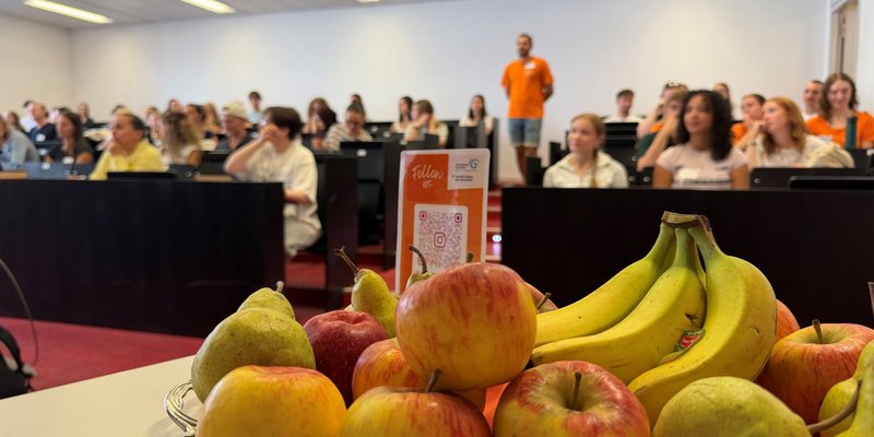 Blick in den gut gefüllten Hörsaal. Im Vordergrund sehen wir frisches Obst, an welchem sich die Teilnehmenden des Campustages SG bedienen dürfen.