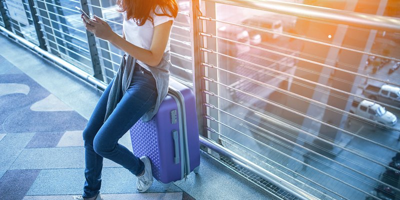 Junge Frau mit Koffer und Rucksack blickt am Flughafen nach vorne und symbolisiert den Start ins internationale Studium
