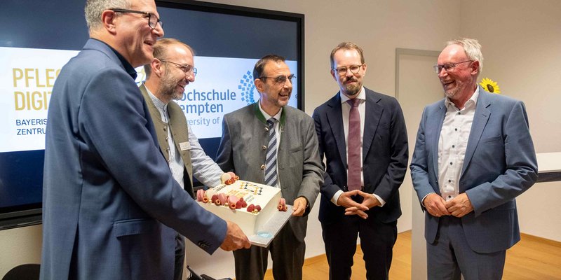 Fünf Männer in Anzügen stehen um eine Geburtstagstorte. 