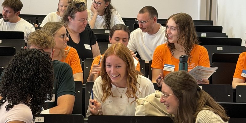 Die Teilnehmenden des Campustages tauschen sich im Hörsaal untereinander aus und zeigen sich lachend die Ergebnisse ihrer Zeichenaufgabe aus der Schnupper-Vorlesung.