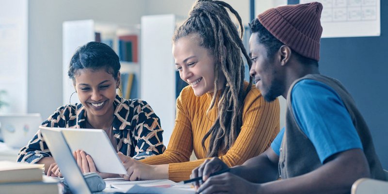 Drei internationale Studierende arbeiten gemeinsam an einem Projekt in moderner Lernumgebung
