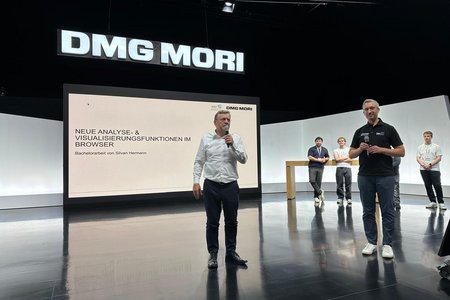Zwei Redner im Vordergrund mit Mikrofonen, drei Studierende im Hintergrund am Hochstisch, daneben die große Leinwand unter dem DMG MORI-Logo