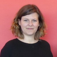 Frau mit schulterlangen braunen Haaren und schwarzem Oberteil vor rotem Hintergrund