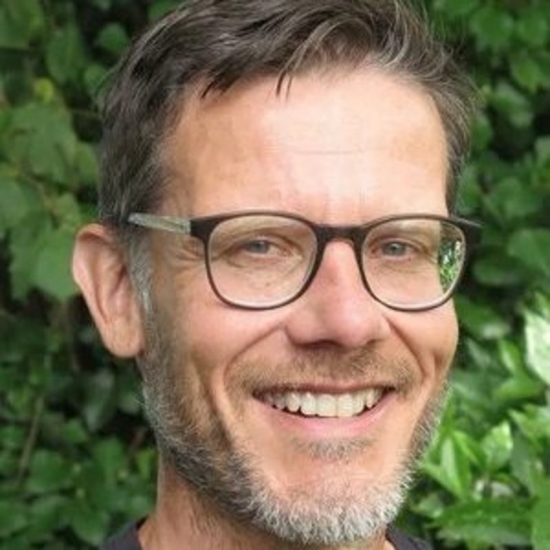 Ein Mann mit kurzen braunen Haaren und Brille lächelt in die Kamera