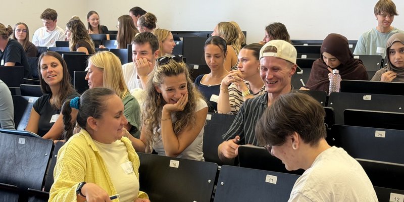 Die Teilnehmenden des Campustages tauschen sich im Hörsaal untereinander aus und zeigen sich lachend die Ergebnisse ihrer Zeichenaufgabe aus der Schnupper-Vorlesung.