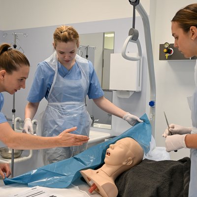Zwei Pflegestudierende werden am Bett mit Simulationspuppe von der Lehrkraft des Skills- und Simulationslabor bei einer Übung zur Körperpflege angeleitet