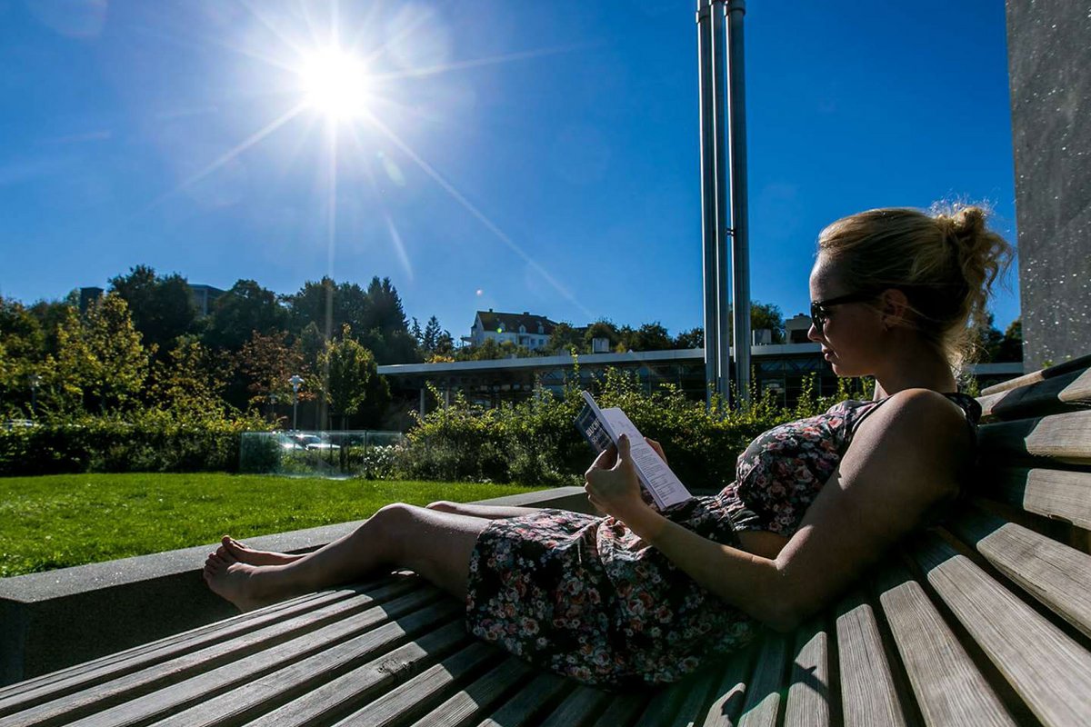 Eine Studentin liest an einem sonnigen Tag vor der Hochschule Kempten ein Buch