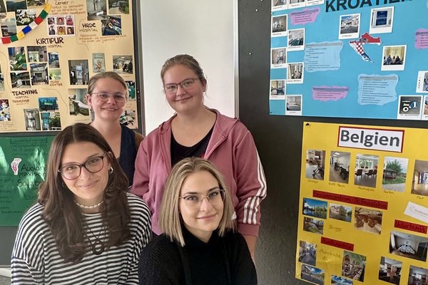 Vier Studierende des Studiengangs Pflege sitzen vor ihren gestalteten Plakaten ihres Auslandspraktikum in Nepal, Kroatien, Belgien und der Schweiz.