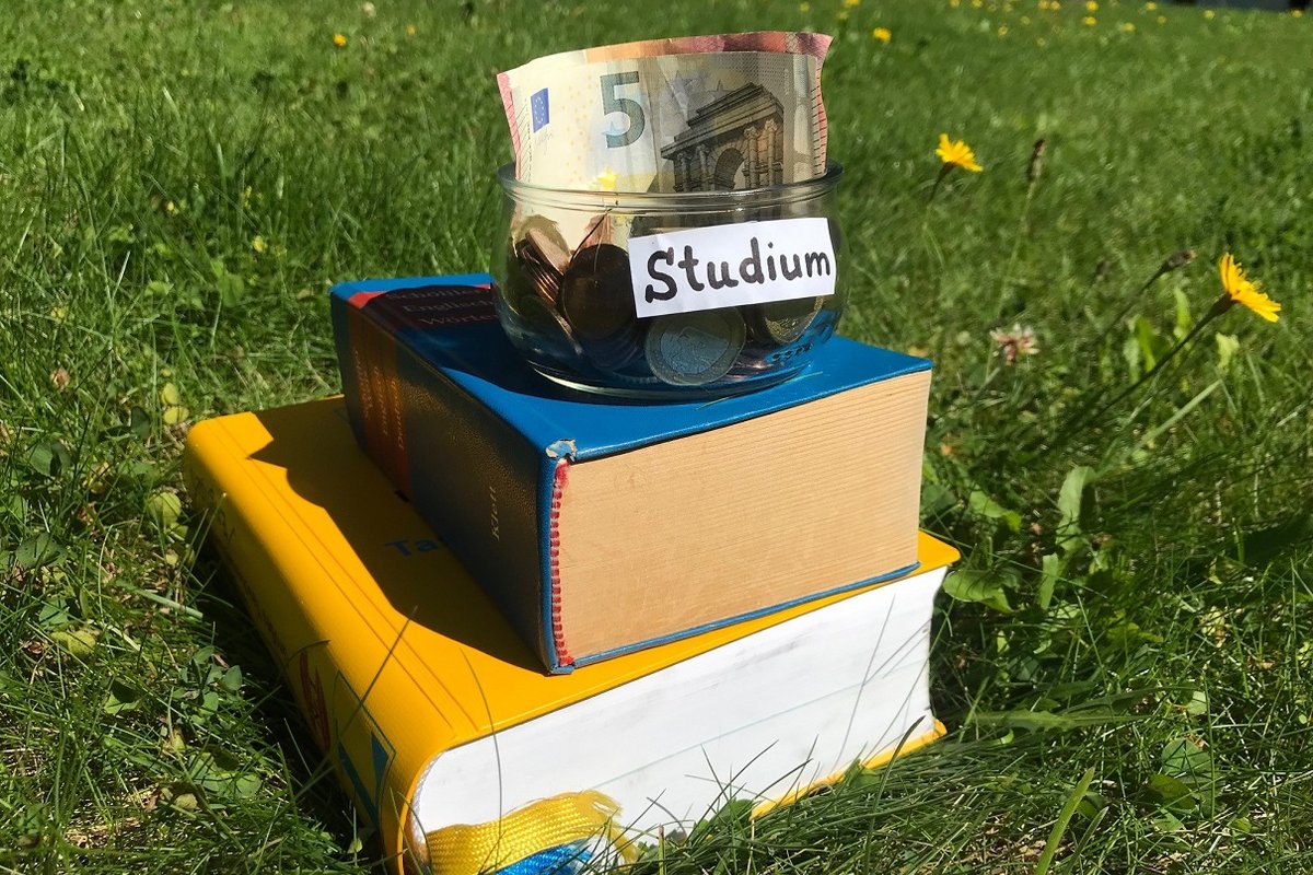 Ein mit „Studium“ beschriftetes Glas mit Münzen und einem Geldschein steht auf Büchern