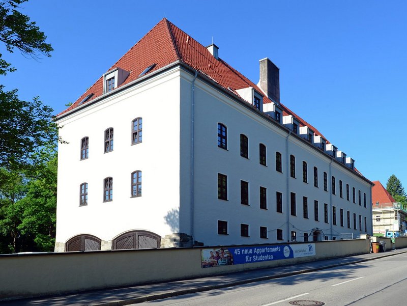 Ein langes, weißes, fünfstöckiges Gebäude mit Schornstein und alten Holzfenstern