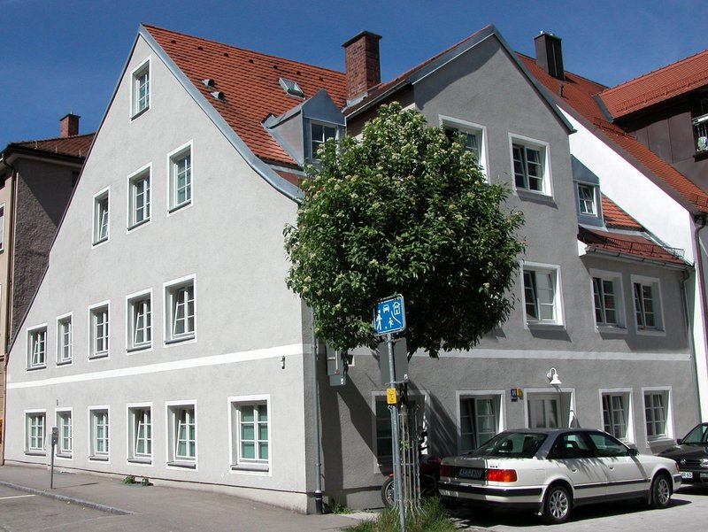 Ein graues, vierstöckiges Haus mit spitz zulaufendem Dach und weissen Details