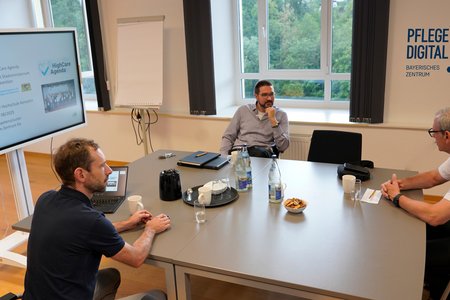 Personen sitzen um einen Tisch mit einem großen Bildschirm