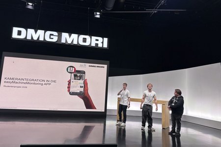 Drei Studierende präsentieren an einem Hochschtisch stehend ihr Projekt, dessen Titel auf einer großen Leinwand daneben zu lesen ist: Kameraintegration in die easyMachinMonitoring APP 
