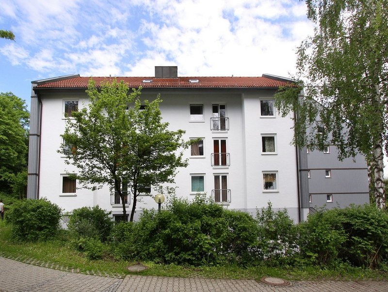 Ein weisses, fünfstöckiges Studierendenwohnheim mit Büschen und Bäumen davor 