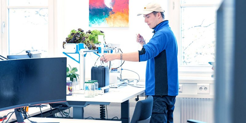In einem Hochschulraum bedient ein Student eine Versuchsanlage zur Aufzucht von Salatpflanzen.