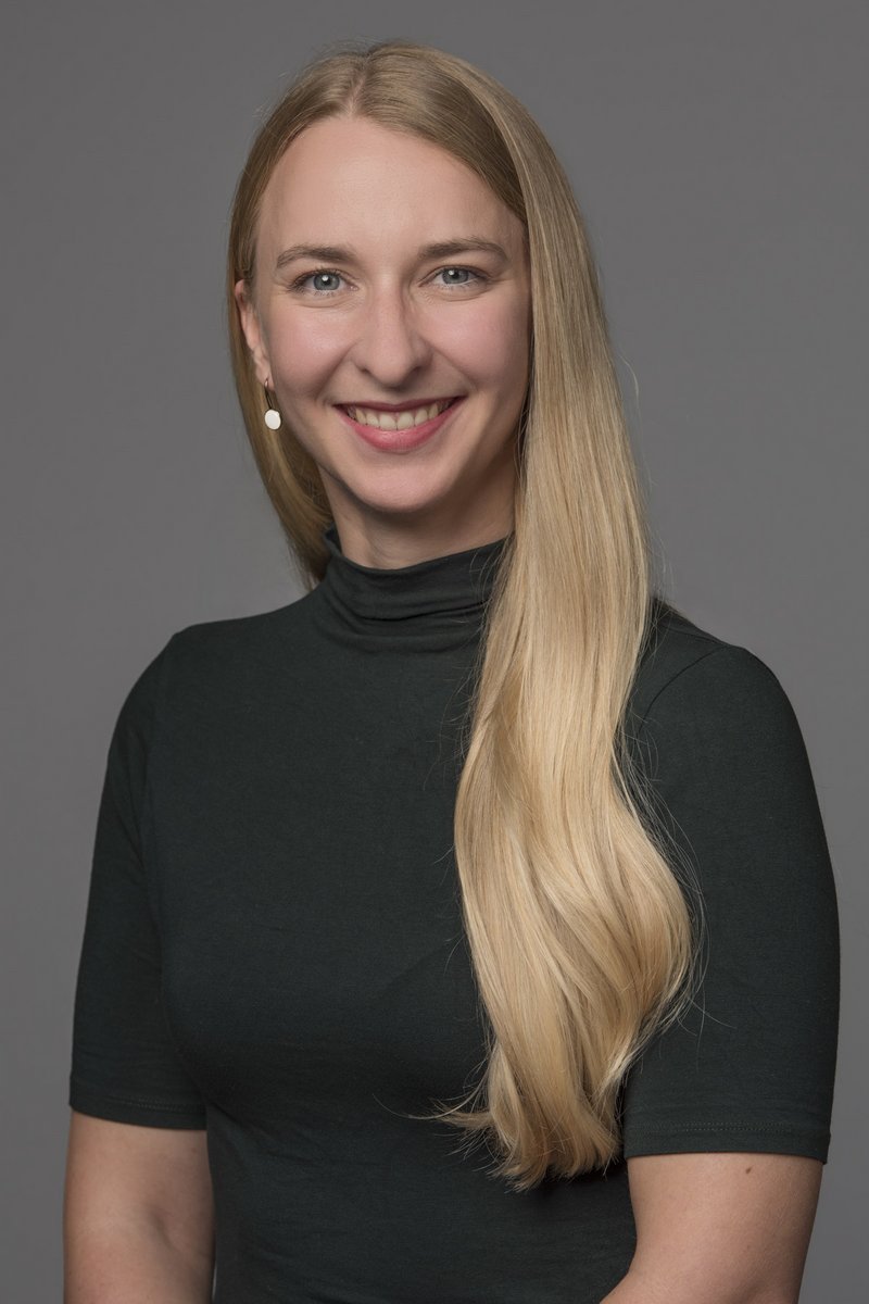 Eine junge Frau mit blonden Haaren und blauen Augen lächelt für ein Portrait in die Kamera