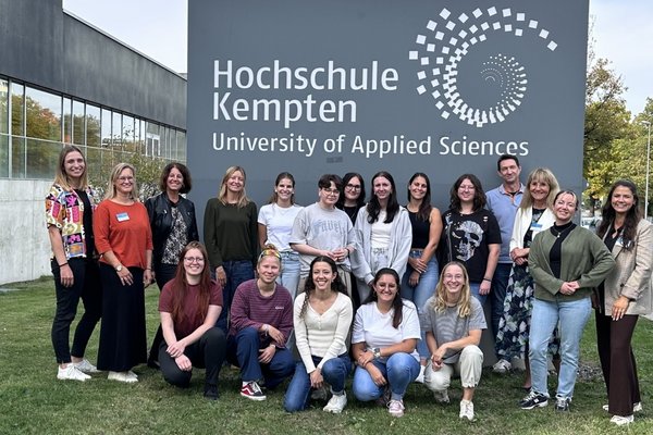 Ein Gruppenbild unserer neuen Pflegestudierenden und dem Team Pflege vor der Hochschulstele aus Stein auf welcher "Hochschule Kempten University of applied Science" steht.