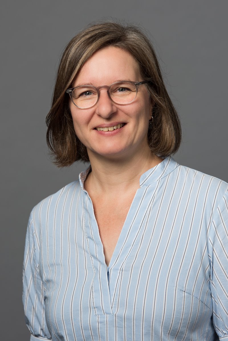 Eine Frau mit kurzen braunen Haaren und Brille lächelt in die Kamera