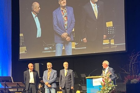 Der Hochschulpräsident hält eine Rede, die drei zu ehrenden Professoren stehen daneben.