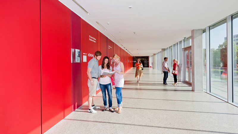 Studierende unterhalten sich auf dem Campus der Hochschule Kempten vor einer roten Wand.