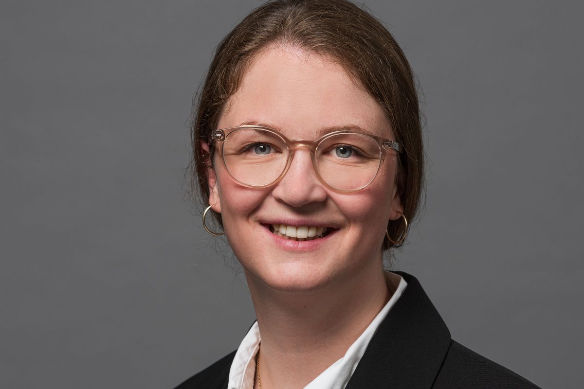 Eine Frau mit braunen Haaren und Brille lächelt in die Kamera