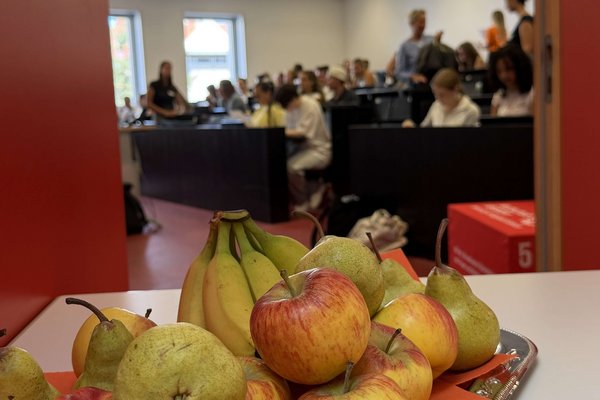 Im Vordergrund ist Obst zu sehen, im Hintergrund unscharf das Innere eines Hörsaals.