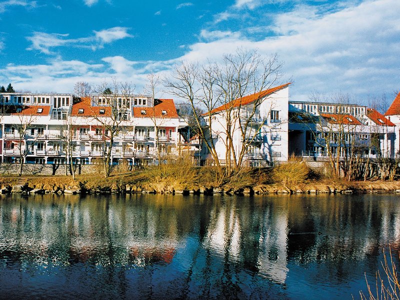Weiße Mehrfamilienhäuser spiegeln sich an einem sonnigen Tag im Fluss Iller