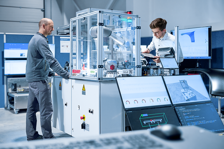 Zwei Mitarbeiter des IPI stehen an einer automatisierten Produktionsanlage. Ein Mitarbeiter erfasst Daten des aktuellen Produktionsprozesses.