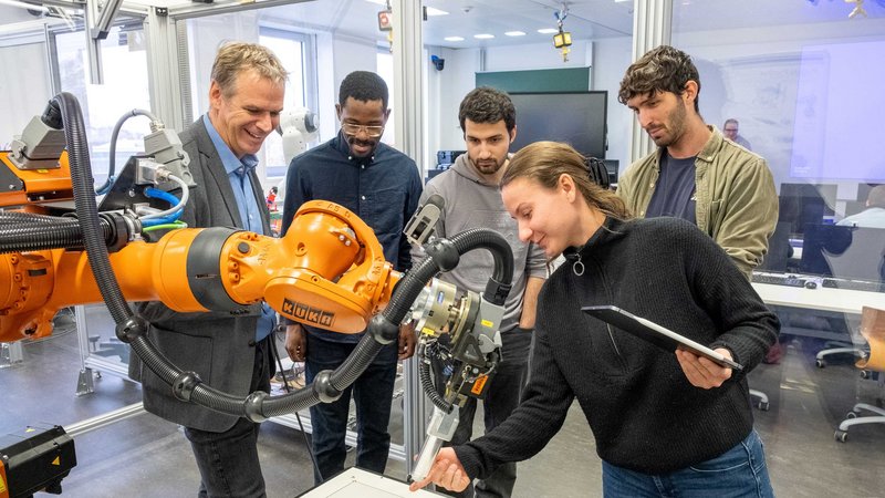 Studierende und Lehrende der Hochschule Kempten arbeiten im Labor mit einem Industrieroboter.
