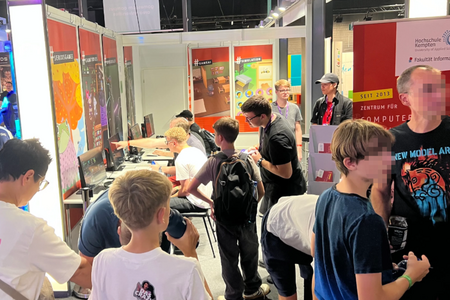 Zahlreiche Besucher am Messestand der Fakultät Informatik und an den Computerplätzen, wo sie Spiele testen.