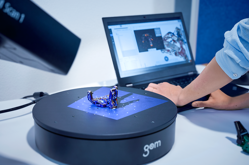 Eine Person scannt mit einem Laptop und einem Scanner ein Bauteil