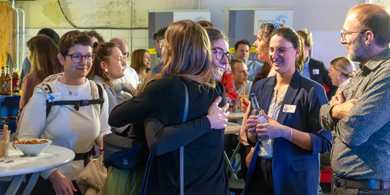 Ein voller Veranstaltungsraum, in der Mitte umarmen sich zwei Frauen. 