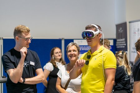 Eine Gruppe um eine Person die mit einer Virtual Reality Brille arbeitet