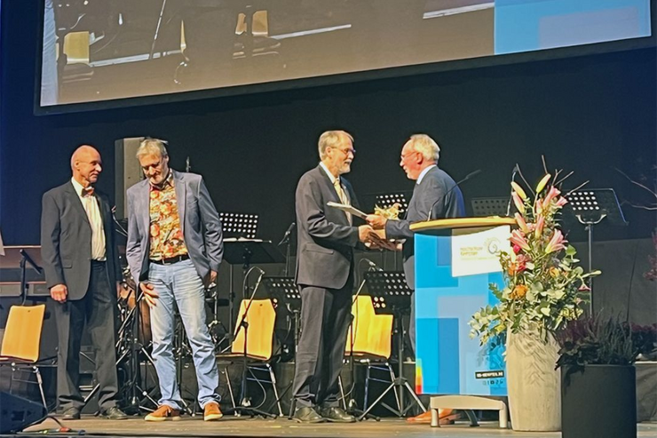 Der Hochschulpräsident überreicht an den bisherigen Dekan ein Geschenk; links stehen zwei weitere Professoren auf der Bühne der BigBox, die geehrt werden.