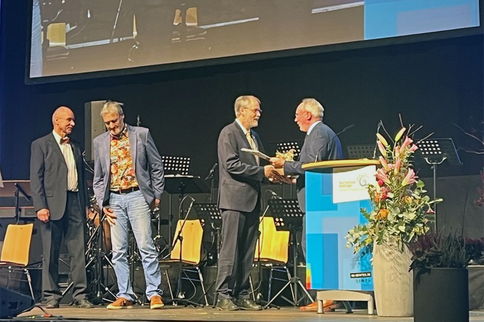 Der Hochschulpräsident überreicht an den bisherigen Dekan ein Geschenk; links stehen zwei weitere Professoren auf der Bühne der BigBox, die geehrt werden.