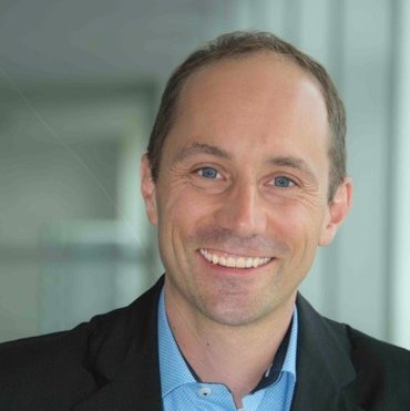 Portrait von einem Mann mit kurzen Haaren, einem schwarzen Anzug und hellblauen Hemd 